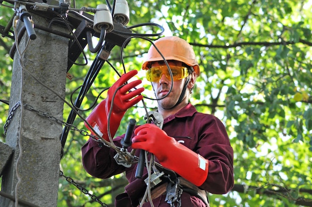 Elektryk na słupie elektrycznym naprawia przewody w linii energetycznej