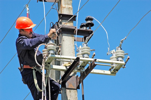 Elektryk na słupie elektrycznym wymienia uszkodzony izolator