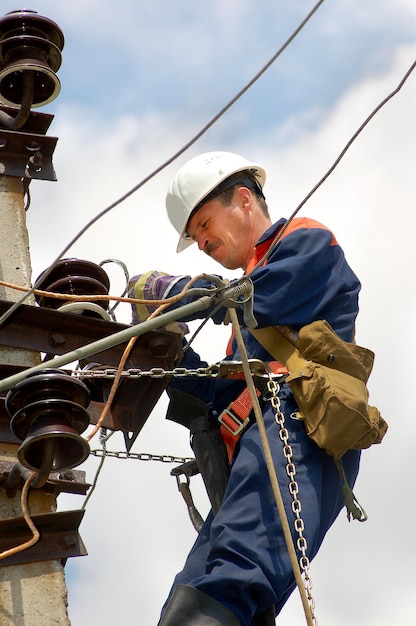 Elektryk na słupie elektrycznym zmienia uszkodzony izolator