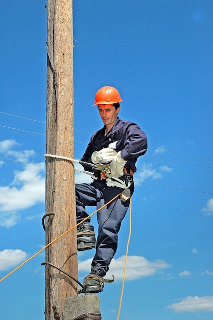 Elektryk w kasku i mundurze wspinający się na drewniany słupek w celu naprawy linii energetycznej