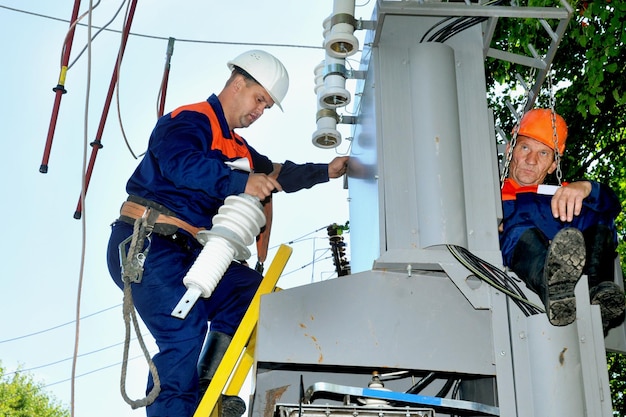 Elektryk w trudno dostępnym miejscu usuwa uszkodzony izolator na podstacji.