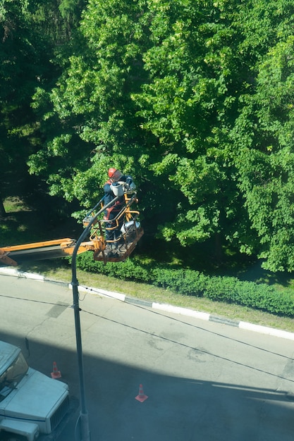 Elektryk wymienia lampę na słupie oświetleniowym, wieża samochodowa podnosi pracownika na słup, aby wymienić żarówkę i pracować.