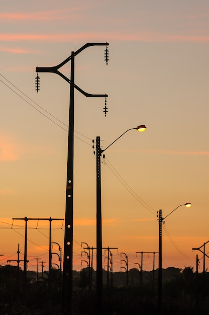 Elektryzujące słupy z pomarańczowym tle zachodu słońca niebo.