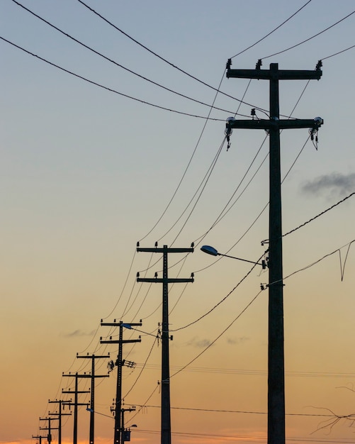 Elektryzujące słupy z pomarańczowym tle zachodu słońca niebo.