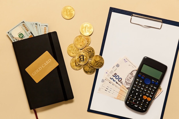 Elementy koncepcji biznesowej na stole złote bitcoiny, dolary, pamiętnik, złota karta, kalkulator na beżowym tle. Bitcoiny to cyfrowa waluta, globalny rynek handlu i wymiany pieniędzy.