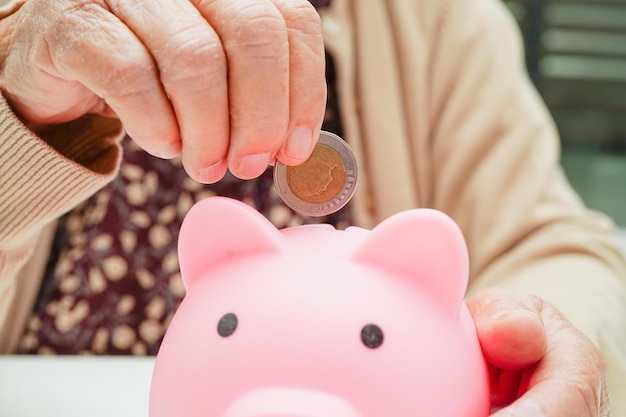 Emerytowana starsza kobieta wkłada monety do skarbonki i martwi się o miesięczne wydatki i opłatę za leczenie