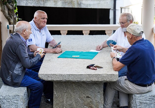 Emerytowani przyjaciele grający w karty przy kamiennym stole w wiosce