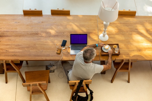 emerytowany mężczyzna trzyma kawę i pracuje na laptopie.