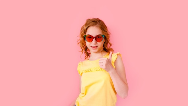 Emocjonalna blondynka nastolatka w błyszczących okularach przeciwsłonecznych i żółtej koszulce śmiejąca się na różowo