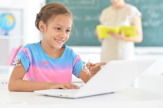 Emocjonalna dziewczynka korzystająca z laptopa siedząc przy biurku w klasie