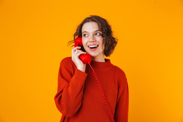 emocjonalna młoda ładna kobieta pozowanie na białym tle na żółtej ścianie rozmawia przez telefon.