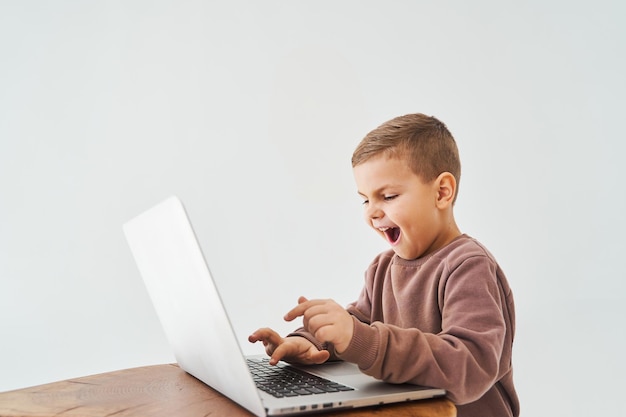 Emocjonalne dziecko gra w gry online na laptopie Uzależnienie od hazardu Przystojny dzieciak gra na laptopie na białym tle