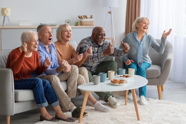 Emocjonalni seniorzy oglądający telewizję w salonie