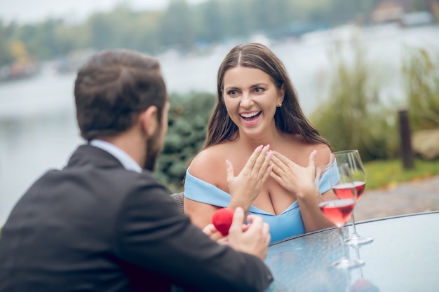 Emocjonalnie zaskoczona entuzjastyczna kobieta z otwartymi ustami i mężczyzna z czerwoną obudową z powrotem do aparatu siedzący w kawiarni na świeżym powietrzu