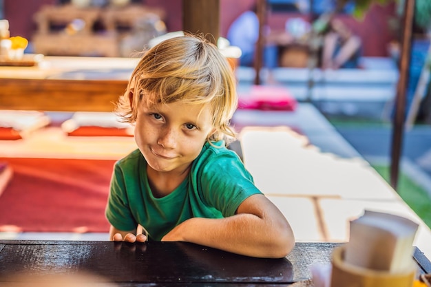 Emocjonalny Chłopiec Przy Stole W Kawiarni śliczny Mały Chłopiec Siedzi W Restauracji Na świeżym Powietrzu W Letni Dzień Dziecko W Kawiarni Czeka Na Jego Zamówienie