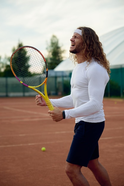 Emocjonalny zawodowy tenisista świętuje zwycięstwo zaciskając pięści. Profesjonalny sportowiec pokazujący wyraz twarzy zwycięzcy, czujący podekscytowanie po wygranej w bardzo napiętej grze