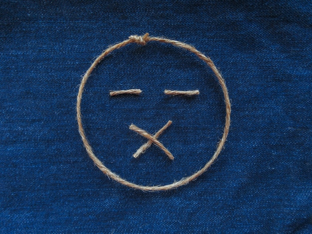 Emoji. Cichy emotikon wykonany ze sznurka na niebieskim denimie. Zbliżenie