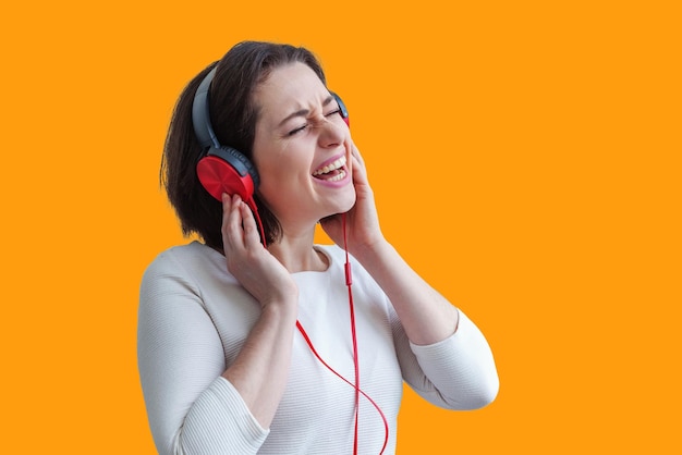 Energiczna młoda brunetka kobieta słucha muzyki w słuchawkach i śpiewa na białym tle na żółtym tle Urocza kaukaska dziewczyna w słuchawkach, ciesząc się muzyką i tańcem z zamkniętymi oczami