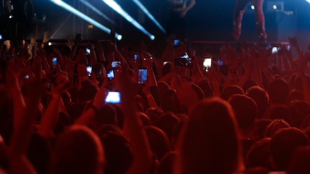 Energiczny tłum tańczący z podniesionymi rękami na koncercie punkowym ciemnoczerwone oświetlenie