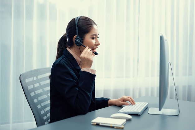 Entuzjastyczne azjatyckie call center ze słuchawkami i mikrofonem pracujące na jej laptopie