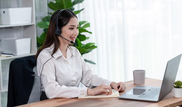 Entuzjastyczne azjatyckie call center ze słuchawkami i mikrofonem pracujące na jej laptopie