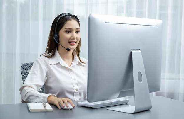 Entuzjastyczne azjatyckie call center ze słuchawkami i mikrofonem pracujące na jej laptopie