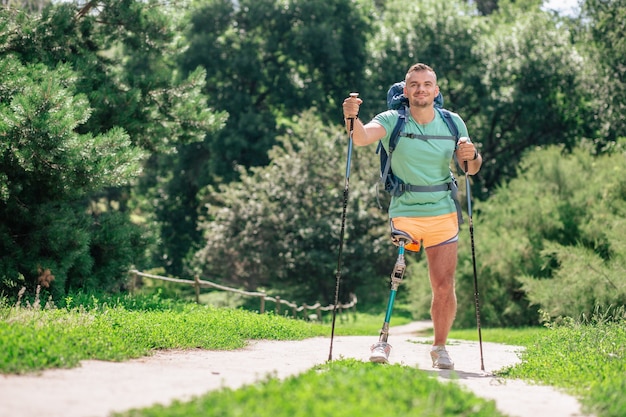 Entuzjastyczny młody człowiek próbujący nordic walking, pozostający aktywnym pomimo trudności