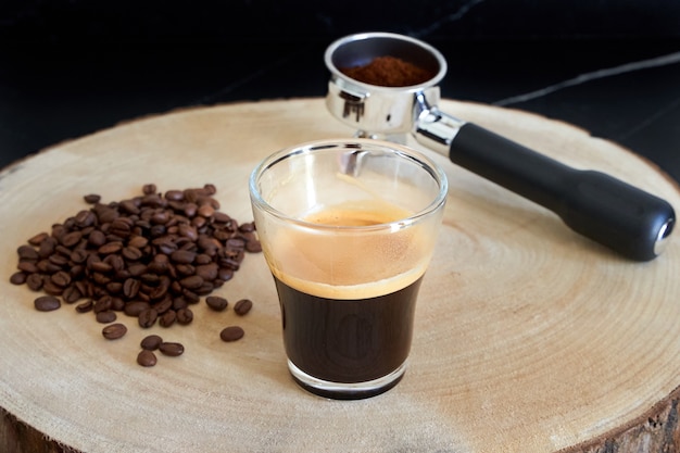 Zdjęcie espresso recien hecho junto a granos de cafe y portafiltros con cafe molido