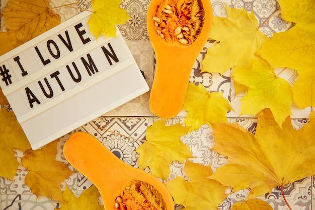 Zdjęcie estetyczne jesienne dekoracje i jedzenie na tle płytek ceramicznych hashtag tekstowy kocham jesień świeże dynie żółte liście widok z góry