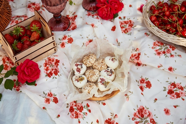Estetyczny letni piknik w słonecznym ogrodzie Różowy obrus pudełko z marshmallows, truskawkami, wiśnią, groszkiem i kieliszkami wina wśród różowych róż Romantyczny wieczór docenienie chwili