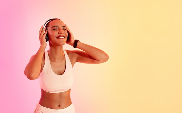 Euphoriczna kobieta z cięciem, ciesząca się muzyką na słuchawkach, nosząca biały biustonosz sportowy