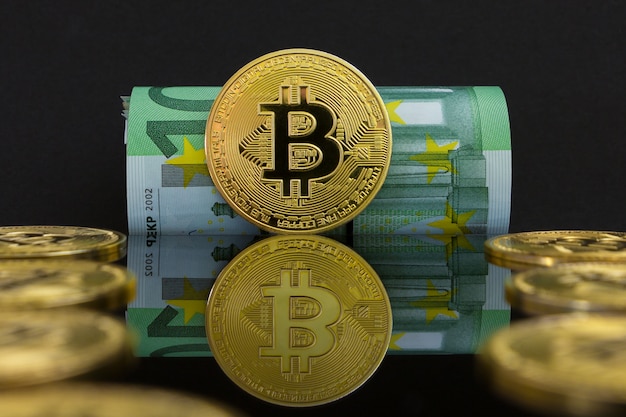 Euro vs kryptowaluta bitcoin. Na czarnym jest sto banknotów euro i duże złote monety btc. Złote bitcoiny nad euro