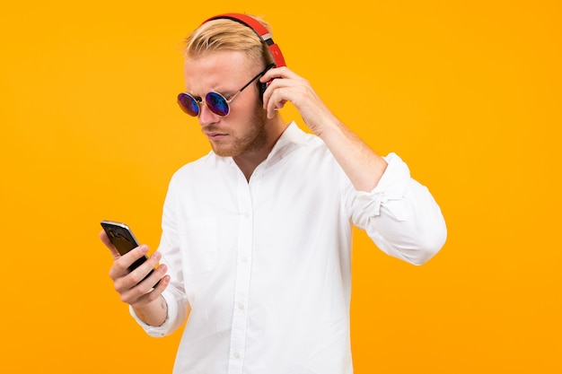 Europejczyk W Białej Koszuli I Okularach Przeciwsłonecznych Z Telefonem Słucha Muzyki W Dużych Słuchawkach Na żółto.