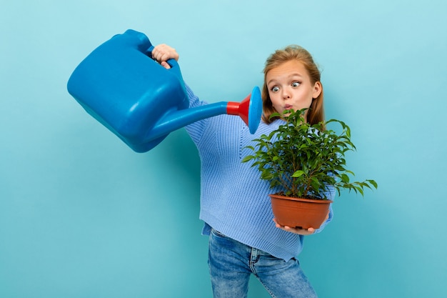 Europejska dziewczyna z konewką i rośliną w jej rękach na jasnoniebieskim