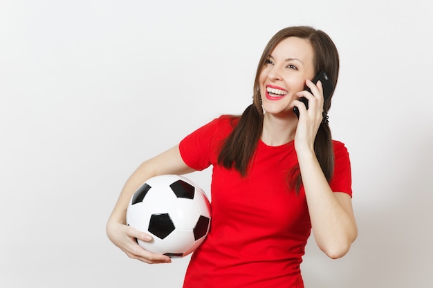 Europejska młoda kobieta, dwa zabawne kucyki, fan piłki nożnej lub gracz w czerwonym mundurze trzymać piłkę nożną, rozmawiać na telefon komórkowy na białym tle. Sport grać w piłkę nożną, koncepcja zdrowego stylu życia.