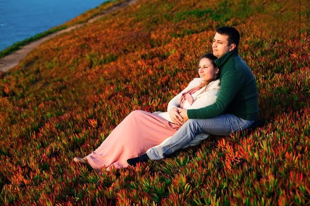 Facet i dziewczyna siedzą na trawie i obejmują się. Podziwiają widok na ocean