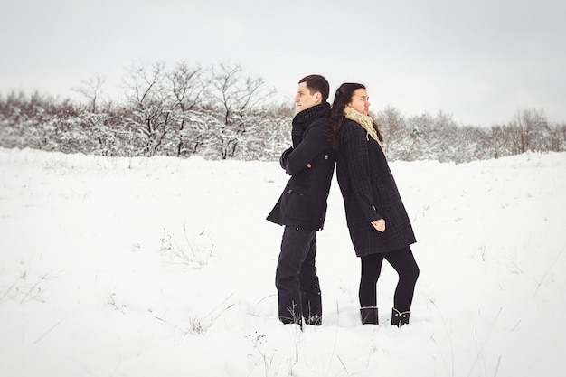 Facet i dziewczyna w ciepłych ubraniach i szalikach na spacerze po zaśnieżonym lesie i na polu