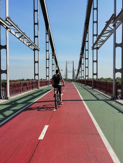 Facet jedzie na rowerze z plecakiem po ścieżce po moście w perspektywie Widok z tyłu