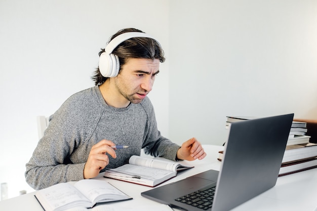 Facet Uczeń Noszący Słuchawki Korzystający Z Laptopa Do Nauki Na Odległość, Cieszący Się Wideokonferencją, Oglądaniem Webinaru, Słuchaniem Kursu Audio, Pisaniem Notatek, Uczeniem Się Z Nauczycielem, Prowadzeniem Lekcji