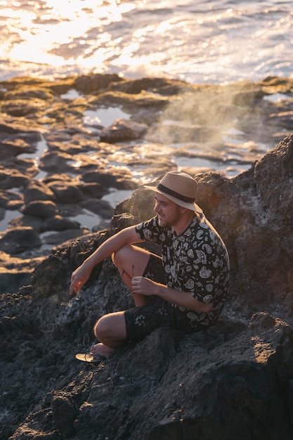 Facet uśmiechający się podczas palenia siedzący na wulkanicznej plaży