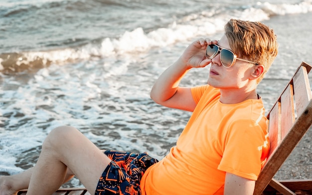 Facet w koszulce i szortach siedzi na leżaku nad morzem