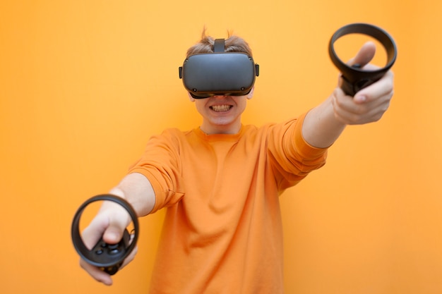 Facet w okularach VR na pomarańczowym tle, gracz trzyma joysticki i gra wirtualną strzelankę