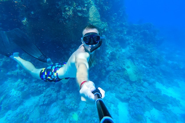 Facet z maską i fajką nurkuje w błękitnej wodzie Morza Czerwonego i fotografuje się