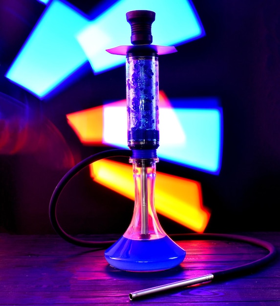 Zdjęcie fajka wodna ze szklaną kolbą i glinianą miską z dymem na neonowym tle