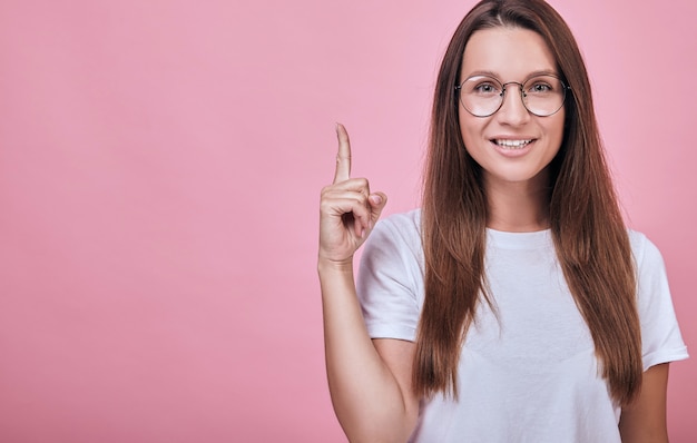 Fajna atrakcyjna kobieta w okrągłych okularach pokazuje palec wskazujący w górę