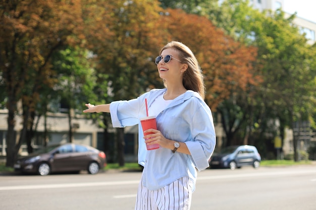 Fajna dziewczyna hipster bawi się na świeżym powietrzu. Wywołanie taksówki w tle miasta.