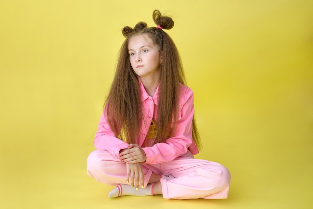 Fajna ładna dziewczyna z modną fryzurą w jasnoróżowych ubraniach siedzi na żółtym tle