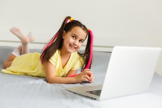 Fajna szkoła online. Dziecko studiuje online w domu za pomocą laptopa. Wesoła młoda dziewczynka przy użyciu komputera przenośnego studiując za pośrednictwem systemu e-learningu online. Nauka na odległość lub zdalna