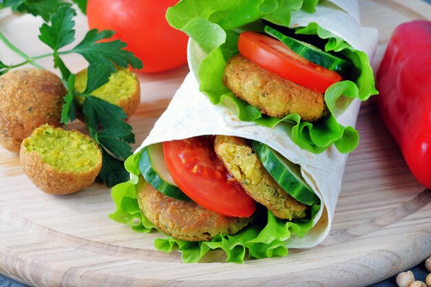 Zdjęcie falafel i warzywa zawinięte w lawasz na lekkiej desce do krojenia.