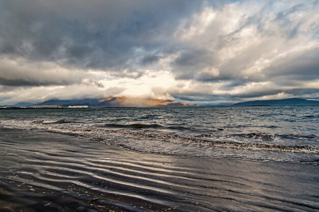 Fale morskie na piaszczystej plaży w reykjaviku, islandia. Seascape z szarą wodą na zachmurzonym niebie. Siła natury. Wanderlust czyli podróże i wakacje.